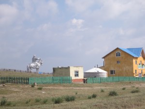 As we approach the gigantic statue, we see a combination of three different types of architecture: the traditional ger, the soviet-style minimalist concrete block house, and a more modern building under construction.