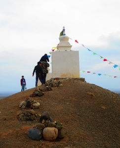 A child on his fathers shoulders places a rock on a stupa.